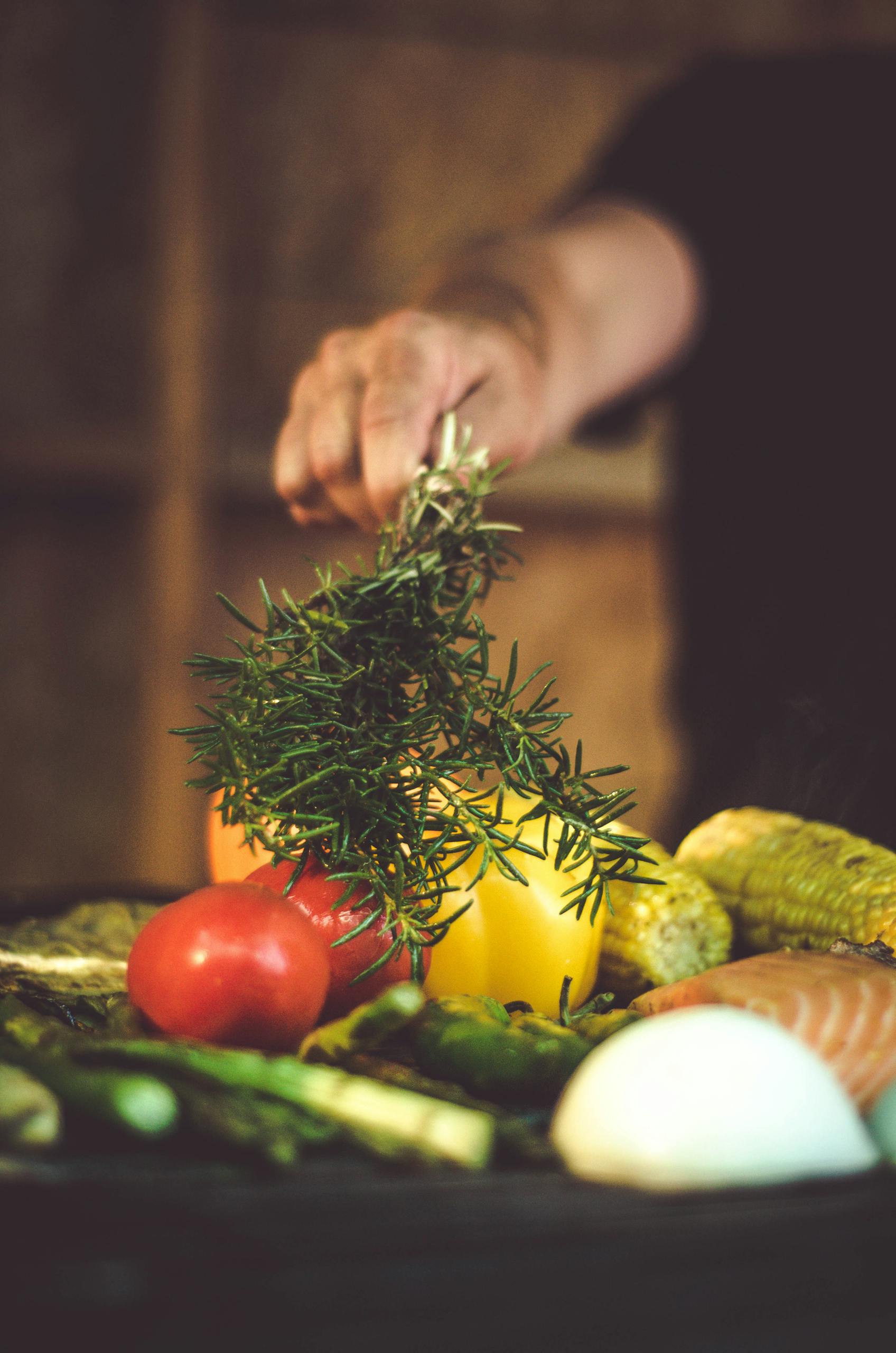 A vibrant assortment of fresh vegetables and herbs, including tomatoes and rosemary, being prepared for grilling.